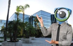 A security guard with a futuristic, AI-inspired EyeQ logo as a head gestures toward a modern glass office building with palm trees. The image symbolizes advanced AI-powered security solutions, reinforcing the need for live video monitoring to protect commercial properties from theft, vandalism, and unauthorized access.