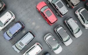 An aerial view of a car dealership lot with multiple vehicles parked in rows. AI-powered dealership security helps prevent test drive thefts and unauthorized lot intrusions using live video monitoring, license plate recognition, and real-time threat detection.