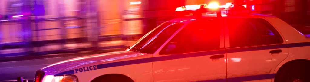 A police car with flashing red and blue emergency lights speeds through a city at night, symbolizing rapid law enforcement response. The image highlights the importance of video-verified alarms in reducing false alerts and ensuring faster police intervention for businesses and commercial properties.