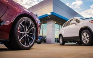 Illustration of a modern automotive dealership lot under 24/7 live video surveillance, highlighting AI-powered virtual guard technology with voice-down deterrence and real-time police dispatch, showcasing smarter dealership security monitoring.